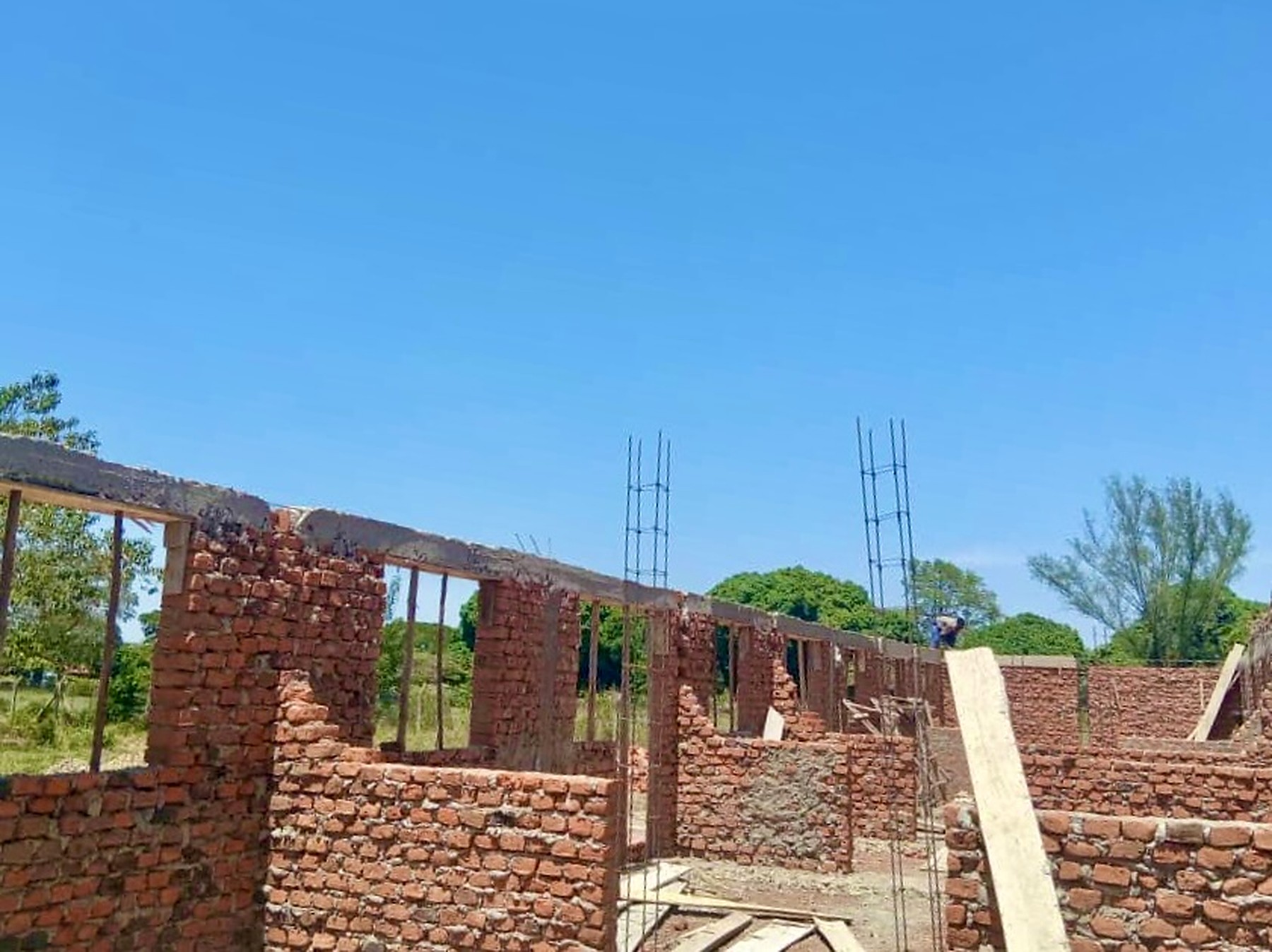 Brick walls with steel reinforcement columns rising for the roof, a builder working in the background